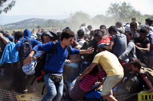 圖為8月31日，難民在希臘和馬其頓邊境的艾杜邁尼檢查站通過鐵絲網進入馬其頓境內。這裡幾乎是亞非難民經由希臘前往馬其頓的唯一「合法」口岸。難民從這裏進入馬其頓不需要什麼證件，邊界兩側的軍警主要是維持秩序。 （新華社 劉詠秋 攝）